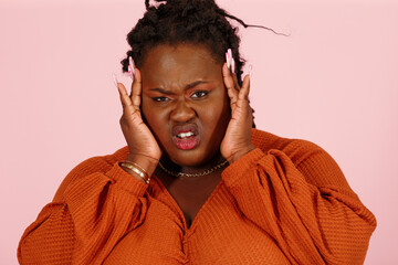 Young black plus size body positive woman patient in orange top suffers from severe headache standing on light pink background in studio closeup
