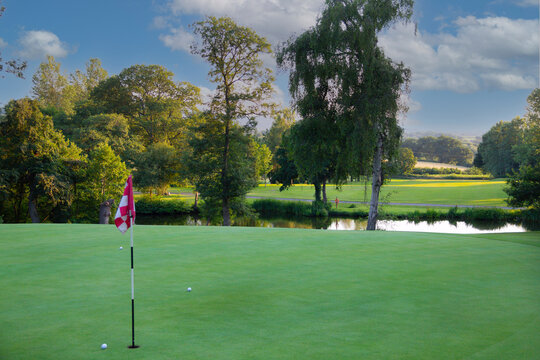 On the green, golf balls sit near the flag on the green at golf course as players hit their balls to try and obtain the treasured hole in one at the sport of golf.