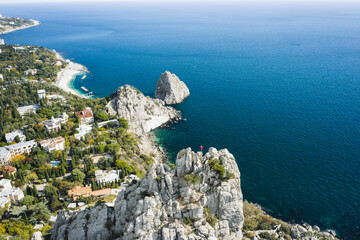 Aerial view of man tourist in red jacket standing on the rock top of cat mountain enjoying landscape of Simeiz with Diva and Penea rocks in background. Crimea