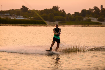 Strong athletic man holds rope and riding wakeboard on water surface.
