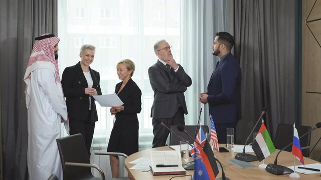 Intercultural delegates discussing points of their colleague speech, multi-ethnic meeting in modern boardroom, everyone in formal wear, sharing opinions.