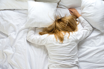 A woman covers her face with a pillow. The woman lies tired on a white bed. Oversleep, not getting...
