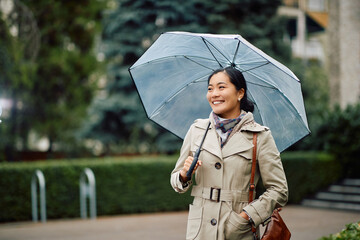 Young happy Asian woman with umbrella walks though the city.