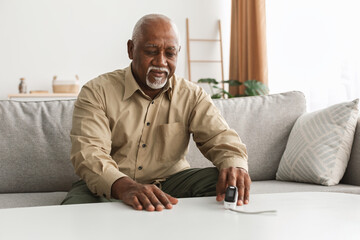 Senior Black Man Measuring Oxygen Saturation Using Pulse Oximeter Indoor