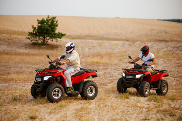 Obraz premium Two men in helmets, atv riding in desert sands
