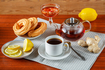 A teapot and a cup of strong aromatic tea on the table on a napkin next to ginger and lemon jam and donuts.