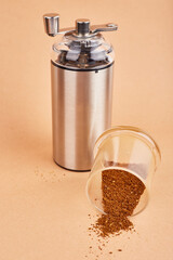 Manual coffee grinder and melted coffee beans on pastel background