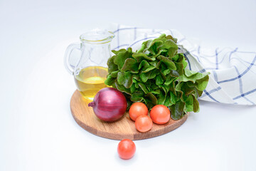 a bunch of green salad, tomatoes, olive oil, ed onion on the wooden board on white background. Ingridients for salad. vegetable salad