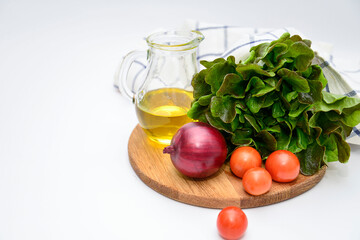 a bunch of green salad, tomatoes, olive oil, ed onion on the wooden board on white background. Ingridients for salad.