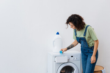 brunette woman adding liquid detergent into washing machine.