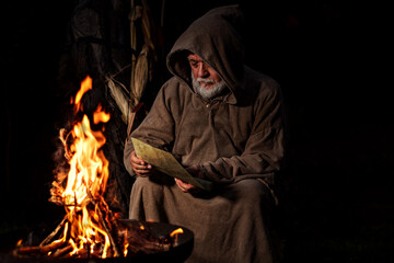 Old medieval man reading message by the fire