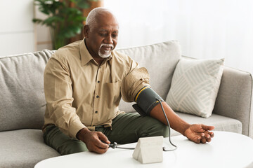 Mature African Man Measuring Arterial Pressure With Medical Device Indoors
