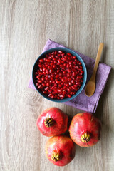 Bowl filled with pomegranate seeds and pomegranate fruit on a table. Flat lay.