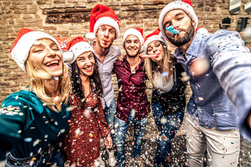 Friends group with santa hats celebrating Christmas taking a selfie - Winter holidays concept with...