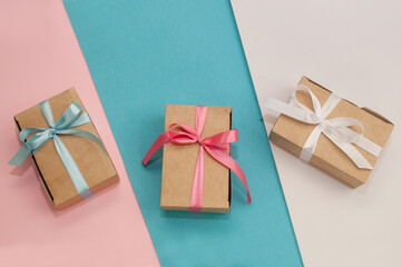 three craft gift boxes tied with white, pink and blue satin ribbons on white, pink and blue backgrounds