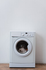 modern washing machine with laundry near white wall.