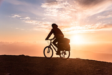 Obraz na płótnie Canvas Mountain bicycle rider with backpack travels over sunrise background