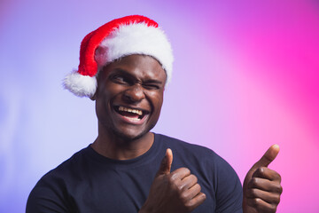 Portrait of positive african american smiling man in santa hat and casual t-shirt on colourful...