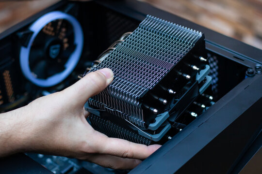 A technician installs an aluminum air-cooled heatsink on a desktop PC CPU. Air Cooler CPU. PC assembly. Technician's hands hold new CPU heatsink. Computer tech background