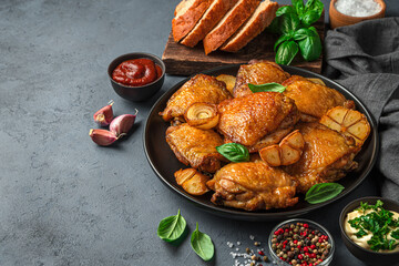 Dinner with fried chicken thighs with garlic, onion and sauces on a dark background.