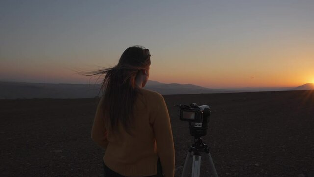 Cinematic shot of a woman filming a sunset close up timelapse with a camera and a tripod in the desert. Slow motion. 