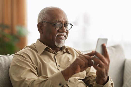 Senior Black Man Texting On Smartphone Using Application At Home