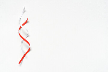 Paper ribbons in twisted white and crimson placed on blank white paper.  Christmas background concept.