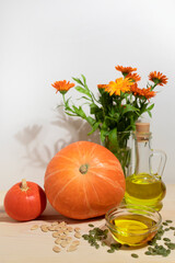 Natural pumpkin seed oil in a bowl and bottle, peeled and unpeeled seeds, pumpkin and calendula flowers on a wooden background, soft focus.