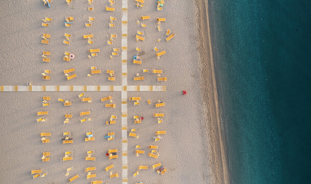 Aerial view of a lido with crossed walkways and closed parasols and sunbeds at sunrise along the coastline in Calabria, Italy.