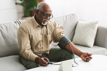 Senior African Male Measuring Arterial Blood Pressure Having Hypertension Indoor