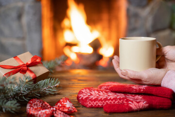 A Christmas gift, women's hands holding a mug of hot mulled wine, red knitted mittens and fir...