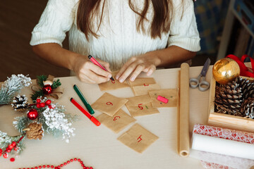 a table with Christmas decorations and the hands of a girl writing numbers on an advent calendar diy