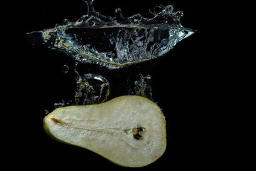 A half of a pear falls into the water on a black background. Pear cut in half. Healthy diet