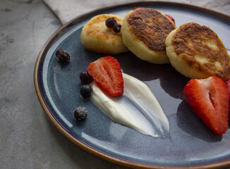 cottage cheese pancakes with strawberries, currant and sour cream on dark blue plate, closeup