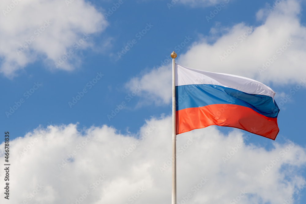 Wall mural The flag of Russia flutters in the wind on a sunny day. Flag of the Russian Federation on a pole against the sky with clouds. Waving Russian tricolor. Copy space