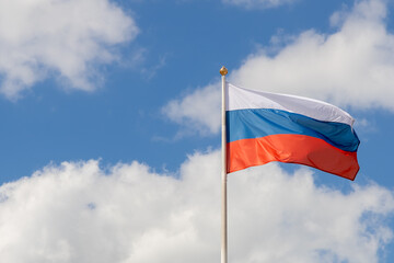 The flag of Russia flutters in the wind on a sunny day. Flag of the Russian Federation on a pole against the sky with clouds. Waving Russian tricolor. Copy space