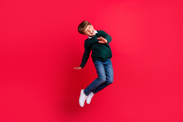 Photo of cute handsome schoolboy dressed green sweater jumping high smiling isolated red color background