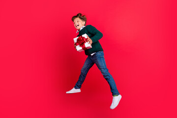 Photo of funky adorable school boy wear knitted pullover smiling jumping high holding present isolated red color background