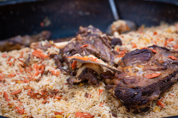 A mountain of delicious rice pilaf with large pieces of meat in a cauldron on a fire in the open air. City picnic. Background with place for text.