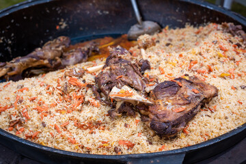 A mountain of delicious rice pilaf with large pieces of meat in a cauldron on a fire in the open air. Street food at mass events. Background with place for text.