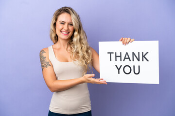 Young Brazilian woman isolated on purple background holding a placard with text THANK YOU and  pointing it