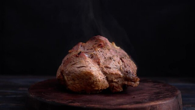 Roasted pork shoulder with steam on cutting board in dark tones. Low light