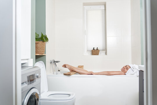 Side view shot of young woman lying in bathtub with her eyes closed. Female relaxing in bathtub. High quality photo