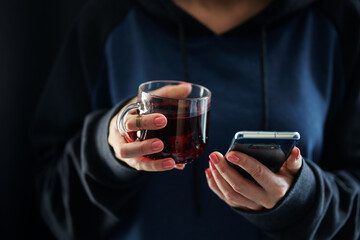 Female hands holding smartphone and cup of tea.