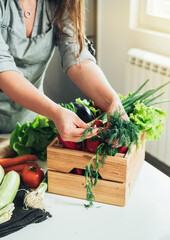 Close Up Photo of Woman Hands Unpacking Fresh Vegetables from Wooden Crate on the Kitchen Table with Copy Space