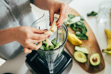 Close Up Photo of Woman Hands Making a Healthy Detox Drink in a Blender - a  Green Smoothie with Bananas, Green Spinach and Avocado. Healthy eating concept, ingredients for smoothies on the table.