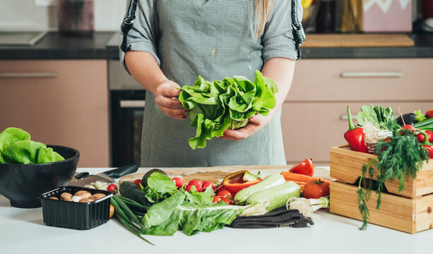 Close Up Photo of Woman Hands Holding Organic Lettuce at Home. 
An anonymous housewife making healthy lunch or seasoning salad at kitchen table full with colorful vegetables.