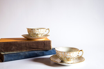 Libros y dos tazas de té pequeñas con adornos de flores doradas pintadas a mano sobre un fondo blanco. Concepto de lectura mientras bebe una bebida herbal tibia y saludable