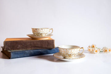Libros y dos tazas de té pequeñas con adornos de flores doradas pintadas a mano sobre un fondo blanco. Concepto de lectura mientras bebe una bebida herbal tibia y saludable
