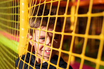 Cheerful young boy on the playground behind the net resting during the game, the boy has a bright smile and happy eyes, he is happy to be among other children, to socialize